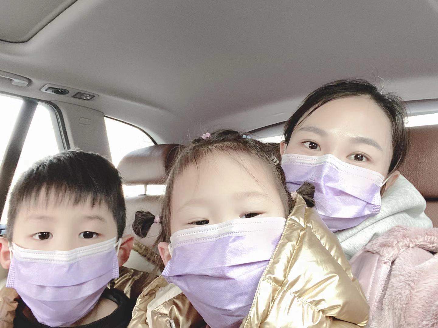 一名妇女和她的两个孩子坐在车里。他们都戴着防护口罩。